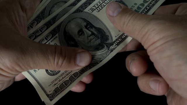 Slow motion of a hand recounting a bundle of hundred-dollar bills on a black background.