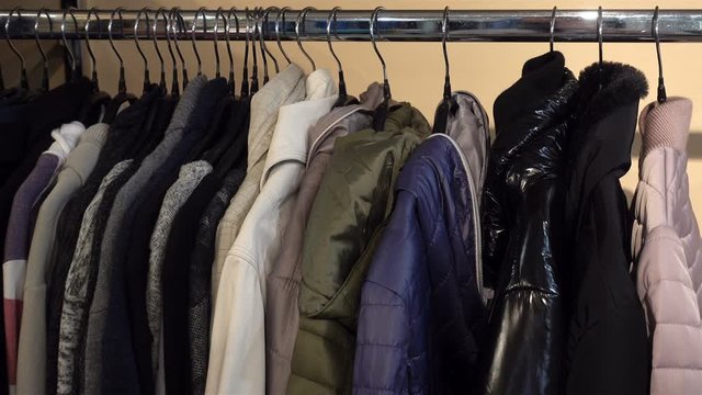 4K view of women's jackets hang on hangers in a row. A hand takes a hanger with a red jacket.