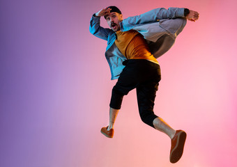 Full length portrait of happy jumping man wearing casual clothes in neon light isolated on gradient background. Emotions, ad concept. Expressive hurrying up, late for work or sale, shopping.