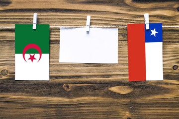 Hanging flags of Algeria and Chile attached to rope with clothes pins with copy space on white note paper on wooden background.Diplomatic relations between countries.