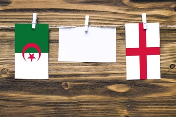 Hanging flags of Algeria and England attached to rope with clothes pins with copy space on white note paper on wooden background.Diplomatic relations between countries.