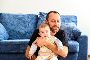 Father sitting on the floor with his baby in his arms in the living room of home.