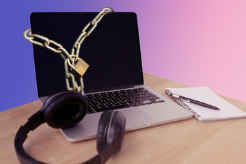 there is an open laptop on the table in the office, on the left on the table are large black headphones, on the right is a notebook with a black pen, a purple background