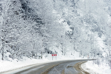 Snowy road scene in winter, with snowy trees, rocks and asphalt road.