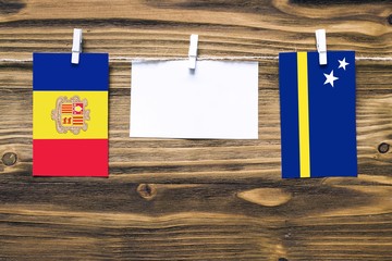 Hanging flags of Andorra and Curacao attached to rope with clothes pins with copy space on white note paper on wooden background.Diplomatic relations between countries.