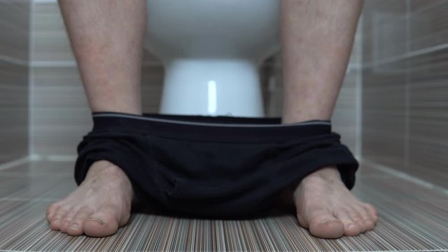 The man took off his black panties while sitting on the toilet. A man with hairy legs in the toilet