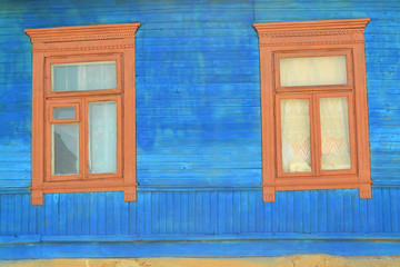 Old wooden windows on a log wall in bright blue. Decoration with carved clypeus.