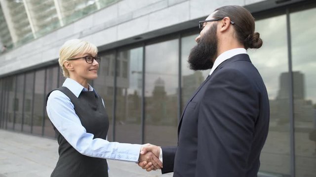 Male and female colleagues shaking hands in street, business cooperation meeting