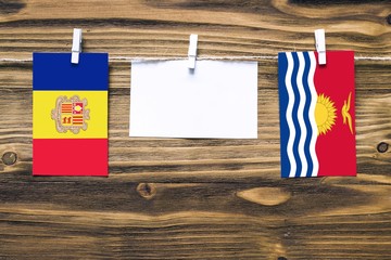 Hanging flags of Andorra and Kiribati attached to rope with clothes pins with copy space on white note paper on wooden background.Diplomatic relations between countries.