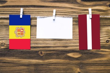 Hanging flags of Andorra and Latvia attached to rope with clothes pins with copy space on white note paper on wooden background.Diplomatic relations between countries.