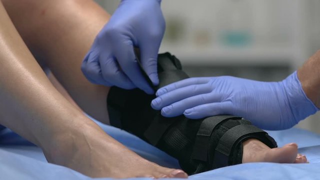 Traumatologist wearing ankle wrap on injured patient leg, trauma treatment