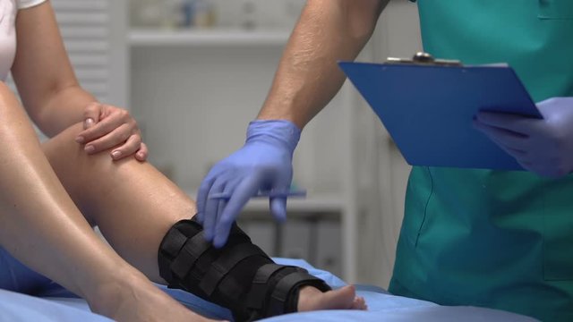 Doctor checking patient leg in ankle wrap, recording examination result, health