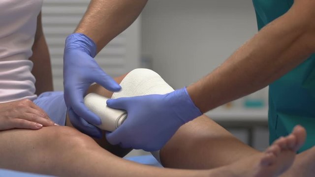 Doctor taking off elastic bandage from patient knee, joint replacement surgery