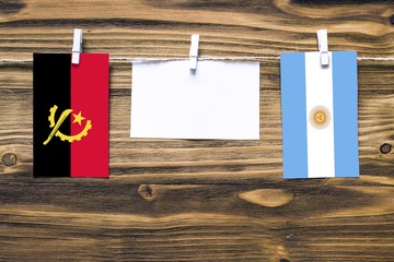 Hanging flags of Angola and Argentina attached to rope with clothes pins with copy space on white...