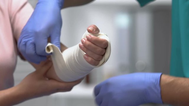 Physician putting elastic bandage on female patient arm, joint dislocation