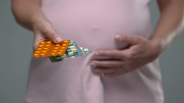 Pregnant lady holding belly showing pills at camera, vitamins for health support