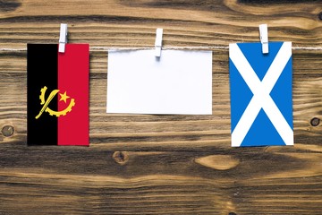 Hanging flags of Angola and Scotland attached to rope with clothes pins with copy space on white...