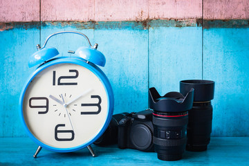 Blue vintage alarm clocks and digital camera on blue wooden table and light blue and pink background wall