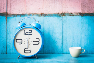 Blue vintage alarm clocks and cup of coffee on blue wooden table and light blue and pink background wall