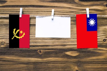 Hanging flags of Angola and Taiwan attached to rope with clothes pins with copy space on white note paper on wooden background.Diplomatic relations between countries.