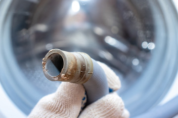 Hand of a plumber holding a broken flexible drain hose of washing machine, clogged and covered with...