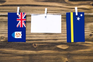 Hanging flags of Anguilla and Curacao attached to rope with clothes pins with copy space on white note paper on wooden background.Diplomatic relations between countries.