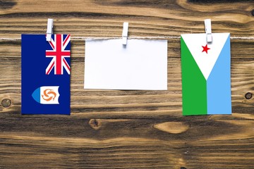Hanging flags of Anguilla and Djibouti attached to rope with clothes pins with copy space on white note paper on wooden background.Diplomatic relations between countries.