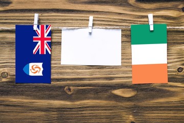 Hanging flags of Anguilla and Ireland attached to rope with clothes pins with copy space on white note paper on wooden background.Diplomatic relations between countries.