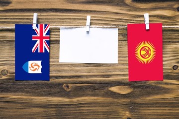 Hanging flags of Anguilla and Kyrgyzstan attached to rope with clothes pins with copy space on white note paper on wooden background.Diplomatic relations between countries.