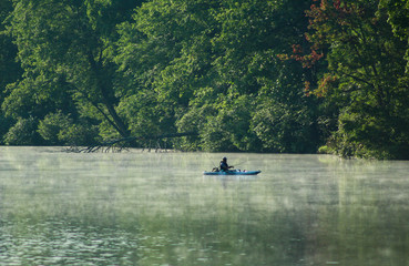 Lone kayaker fishing on the early morning lake
