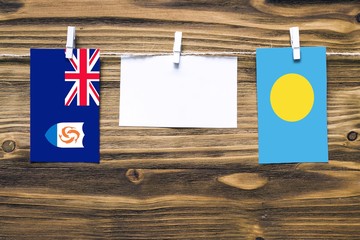 Hanging flags of Anguilla and Palau attached to rope with clothes pins with copy space on white note paper on wooden background.Diplomatic relations between countries.