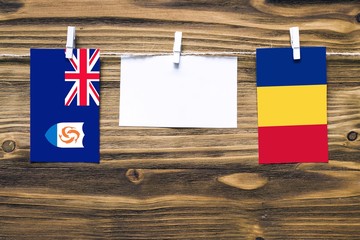 Hanging flags of Anguilla and Romania attached to rope with clothes pins with copy space on white...