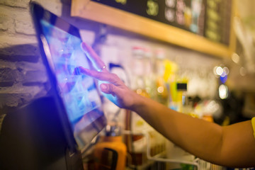 Blurry picture of cashier is making order on touch screen of computer in cafe or store. Barista is using the screen to receive orders from customers who are pointing to order coffee.