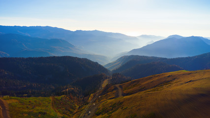 Beautiful aerial view to the evening mountains in Sochi Roza Hutor. Picturesque motion of autumn valley with the sun behind the peaks and hazy sunshine.