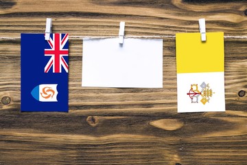 Hanging flags of Anguilla and Vatican City attached to rope with clothes pins with copy space on white note paper on wooden background.Diplomatic relations between countries.