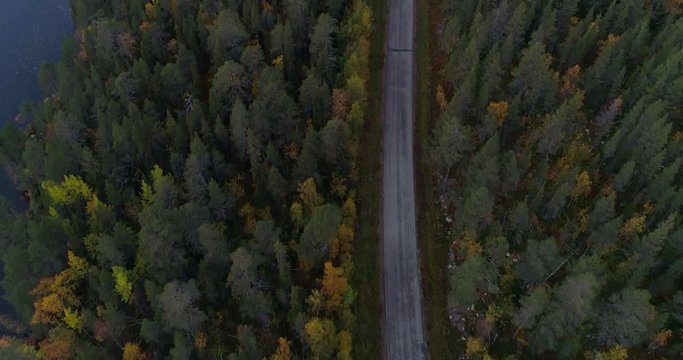 Lapland forest road, Aerial, tilt up, drone shot, over a camper paked on a asphalt route, at lake Jerisjarvi, in middle of fall colored trees, on a cloudy, autumn day, in Pallas-Yllas park, Finland