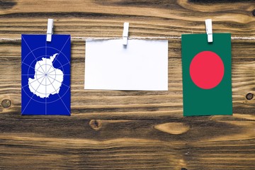 Hanging flags of Antarctica and Bangladesh attached to rope with clothes pins with copy space on white note paper on wooden background.Diplomatic relations between countries.