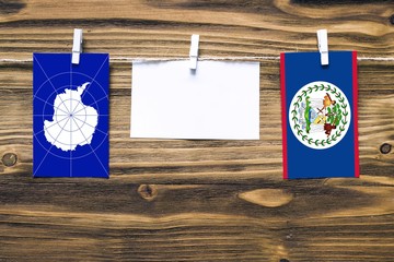 Hanging flags of Antarctica and Belize attached to rope with clothes pins with copy space on white note paper on wooden background.Diplomatic relations between countries.