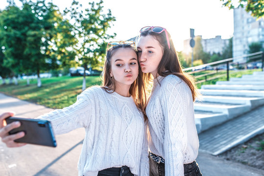 Two girls schoolgirls teenagers 12-15 years old, in autumn summer day city, in hands of smartphone, selfie photo, video call, sweaters in everyday clothes. Emotions joy, fun, happy smiling.