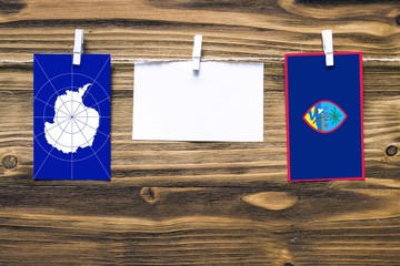 Hanging flags of Antarctica and Guam attached to rope with clothes pins with copy space on white note paper on wooden background.Diplomatic relations between countries.