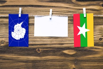 Hanging flags of Antarctica and Myanmar attached to rope with clothes pins with copy space on white note paper on wooden background.Diplomatic relations between countries.