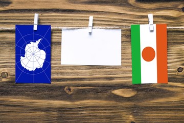 Hanging flags of Antarctica and Niger attached to rope with clothes pins with copy space on white note paper on wooden background.Diplomatic relations between countries.