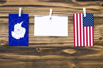 Fototapeta na wymiar Hanging flags of Antarctica and United States attached to rope with clothes pins with copy space on white note paper on wooden background.Diplomatic relations between countries.