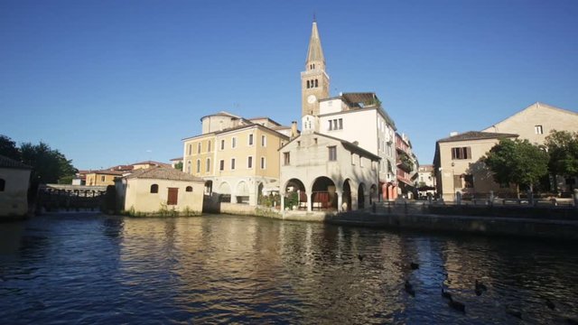 Catholic oratory of Madonna della Pesqueria and belfry of St. Andrew Cathedral on bank on Lemene river in Portogruaro, Veneto, Italy