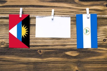 Hanging flags of Antigua and Barbuda and Nicaragua attached to rope with clothes pins with copy space on white note paper on wooden background.Diplomatic relations between countries.