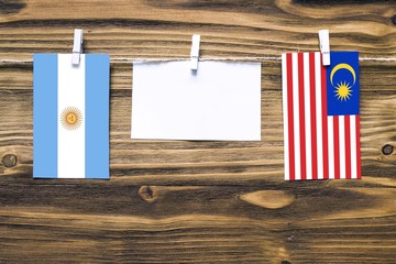 Hanging flags of Argentina and Malaysia attached to rope with clothes pins with copy space on white note paper on wooden background.Diplomatic relations between countries.