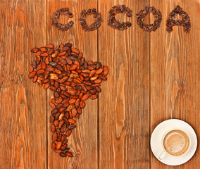 South America continent made of cocoa beans, the word "cocoa" made of cacao nibs with cup of cacao drink on wooden background. Top view.