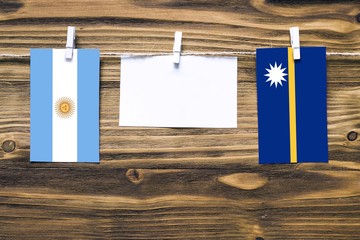 Hanging flags of Argentina and Nauru attached to rope with clothes pins with copy space on white note paper on wooden background.Diplomatic relations between countries.