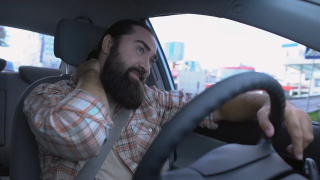 Bearded man suffers neck pain while driving car, muscle spasm, inflammation