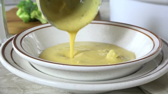 Ladling creamy broccoli cheese bisque into a bowl slow motion